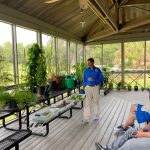 279459331_5123309661061254_2085035167156009300_n A man in a blue shirt teaches a group of people about plant identification while in an outdoor classroom.