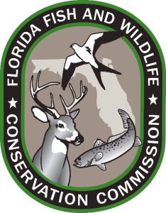 Florida Fish and Wildlife Conservation Commission logo which contains a spotted fish, deer with antlers, and swallowtail kite bird over a silhouette of the state of Florida, all light brown and grey, encircled by black and green lines and white text that reads the name of the organization
